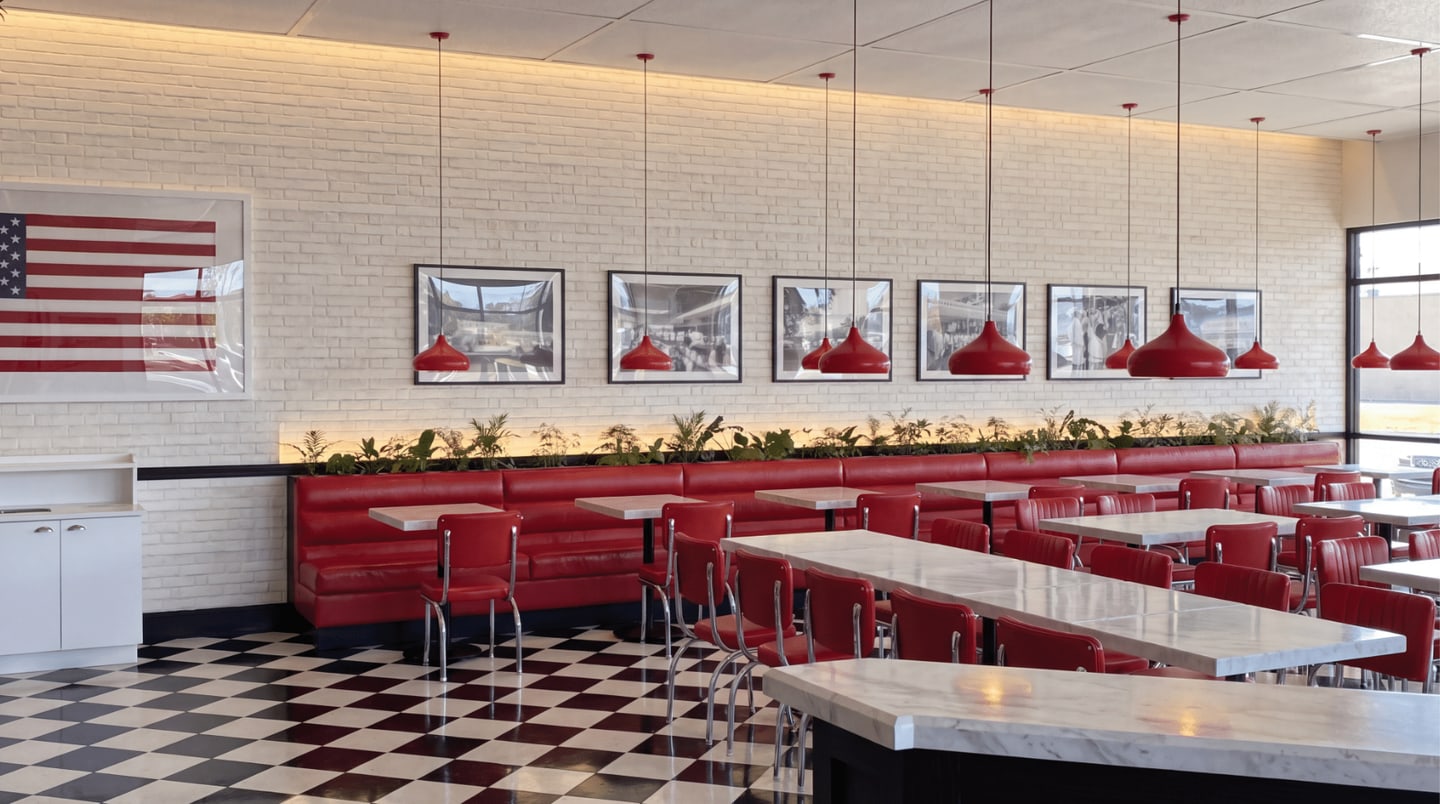 Steak ’n Shake dining room with red banquette seating, pendant lights, an American flag, and framed wall art